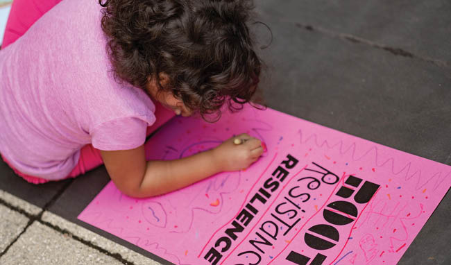 Child drawing poster on sidewalk